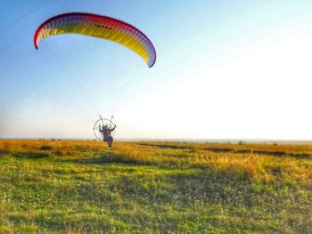 Man flying powered parachute over grassy field against clear sky