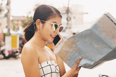 Smiling mid adult woman with world map using phone on street