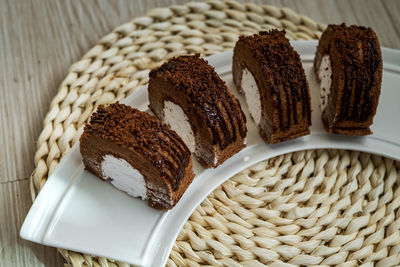 Chocolate roll with fresh cream on a white plate and wooden background