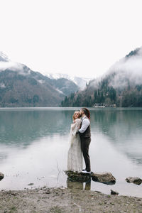 Two happy people in love the bride and groom in wedding outfits embrace by the lake and mountains