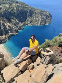 Young man sitting on rock with view of blue ocean 