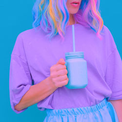 Midsection of woman holding drink jar against colored background