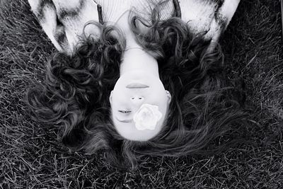 Directly above portrait of woman with rose on eye lying at grassy field