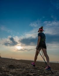 Rear view of woman standing on beach against sky during sunset