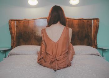 Rear view of woman sitting on bed