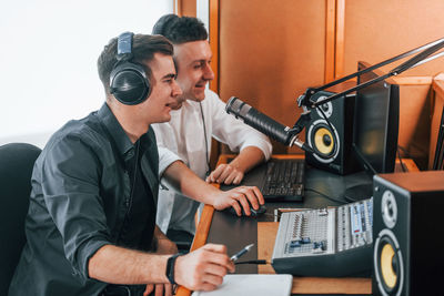 Two guys is indoors in the radio studio is busy by broadcast.