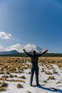 Rear view of man standing on snowcapped mountain against clear blue sky