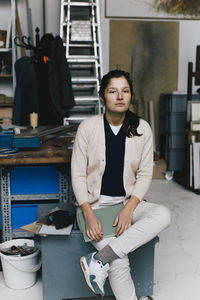 Portrait of businesswoman sitting on table in workshop