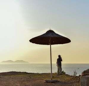 Man photographing woman standing on beach against clear sky