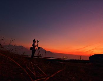 Silhouette person photographing on land against sky during sunset