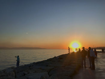 Silhouette people on beach against sky during sunset