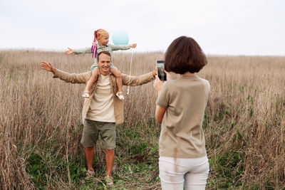Mom takes pictures of happy dad and daughter in summer nature on smartphone. family with small child