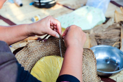 Close-up hands of thai female artisans is using a needle weaving sew hat woven