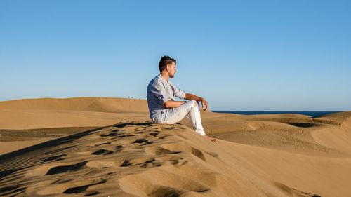 Young woman standing on sand at desert against clear sky