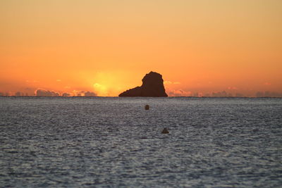 Silhouette rocks on sea against sky during sunset