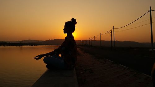 Silhouette of woman meditating against sky during sunset