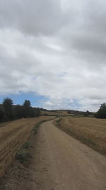 Road by agricultural field against sky