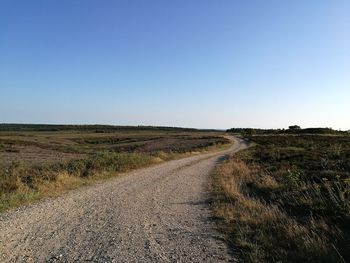 Empty road amidst field against clear sky