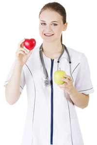 Portrait of nurse holding apple and heart shape against white background