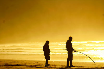 Silhouette men standing on beach against sky during sunset