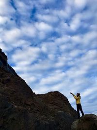Low angle view of woman pointing while standing on mountain against cloudy blue sky