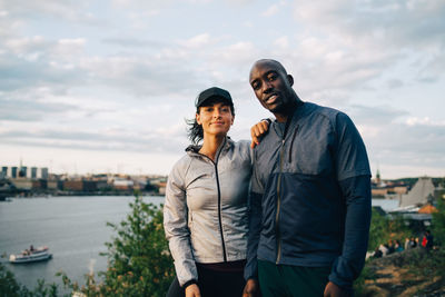 Portrait of confident male and female athlete standing on hill against sky
