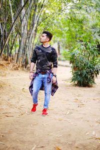 Full length portrait of young man standing against trees
