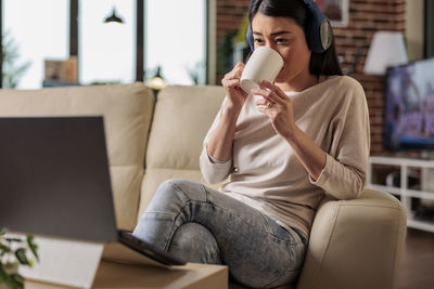 Young woman using phone while sitting on sofa at home