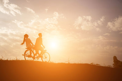 Silhouette people riding bicycle on field against sky during sunset