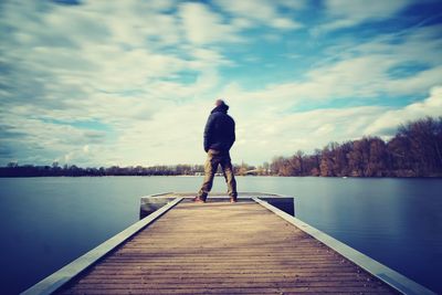 Rear view of man standing on pier over lake against sky