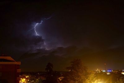 Lightning over illuminated cityscape against sky at night