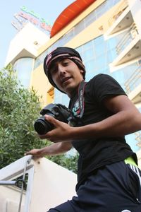 Young man holding camera while standing against building