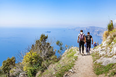 Rear view of people walking on mountain against sky