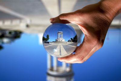 Cropped hand of woman holding crystal ball against built structure