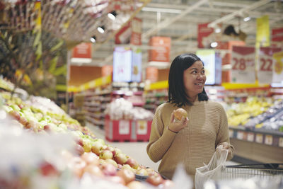 Smiling woman standing in supermarket and holding apple