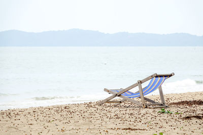 Deck chairs on beach against sky