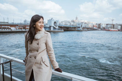 Portrait of young woman standing against river