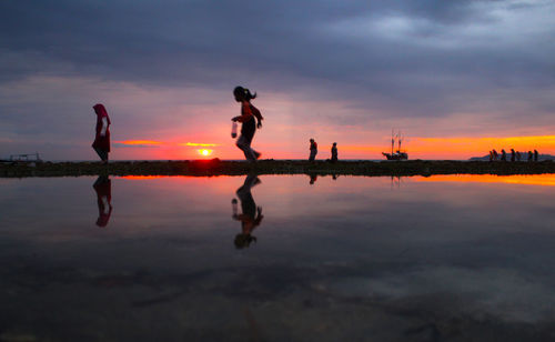 Silhouette men on water against sky during sunset