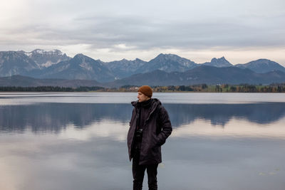 Man looking away while standing against lake