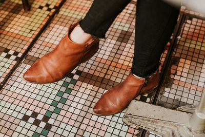 Low section of woman wearing brown shoes on tiled floor
