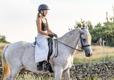 White lusitano mare, female dressage rider, outdoors on sand.