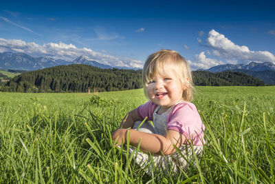Portrait of smiling cute girl sitting on grass against sky