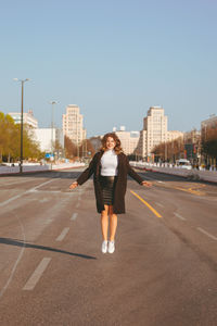 Full length of woman in mid air on city street against clear blue sky