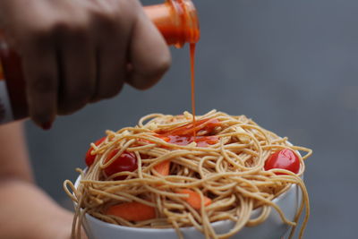 Cropped hands pouring sauce on noodles