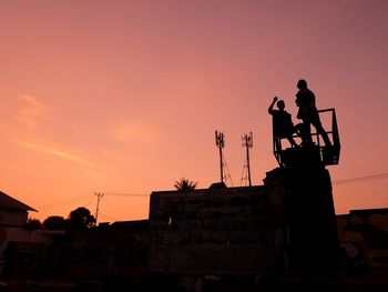 Silhouette man statue by building against sky during sunset