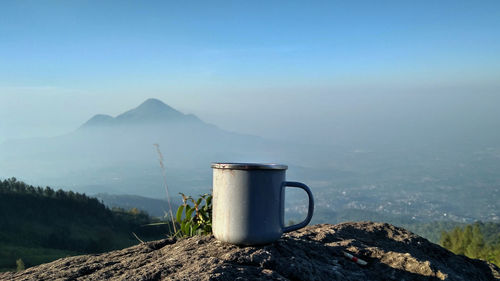 Coffee cup on rock against sky