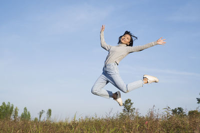 Full length of young woman jumping on field against sky