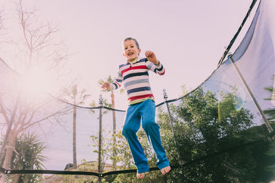 Low angle view of boy jumping on trampoline against trees