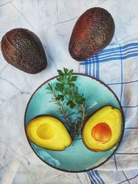 Fresh avocado with herbs and lemons lies on the table on blue plate on white background. flat lay