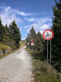 Road sign by trees against sky